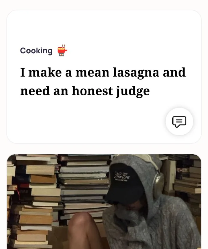 An Alyke profile card for Cooking that reads: I make a mean lasagna and need an honest judge, above a photo of the member in a cap and hoodie sitting among stacks of books
