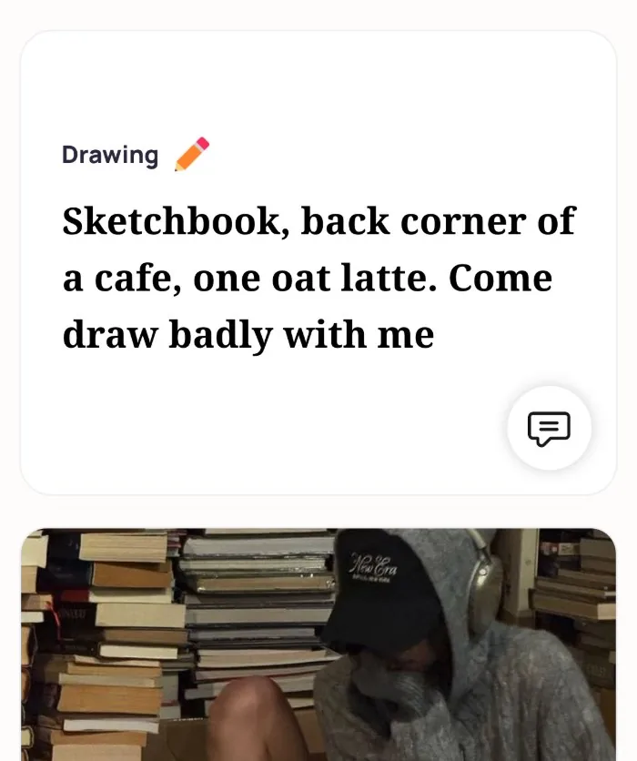 An Alyke profile card for Drawing that reads: Sketchbook, back corner of a cafe, one oat latte. Come draw badly with me, above a photo of the member in a cap and headphones among stacks of books