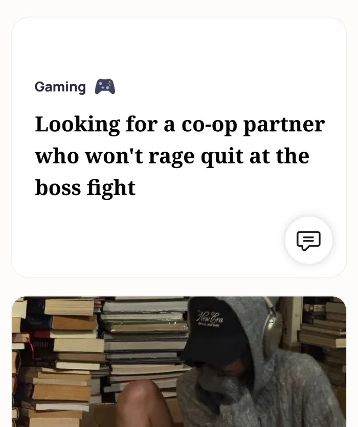 An Alyke profile card for Gaming that reads: Looking for a co-op partner who won't rage quit at the boss fight, above a photo of someone in a hoodie and cap sitting among stacks of books