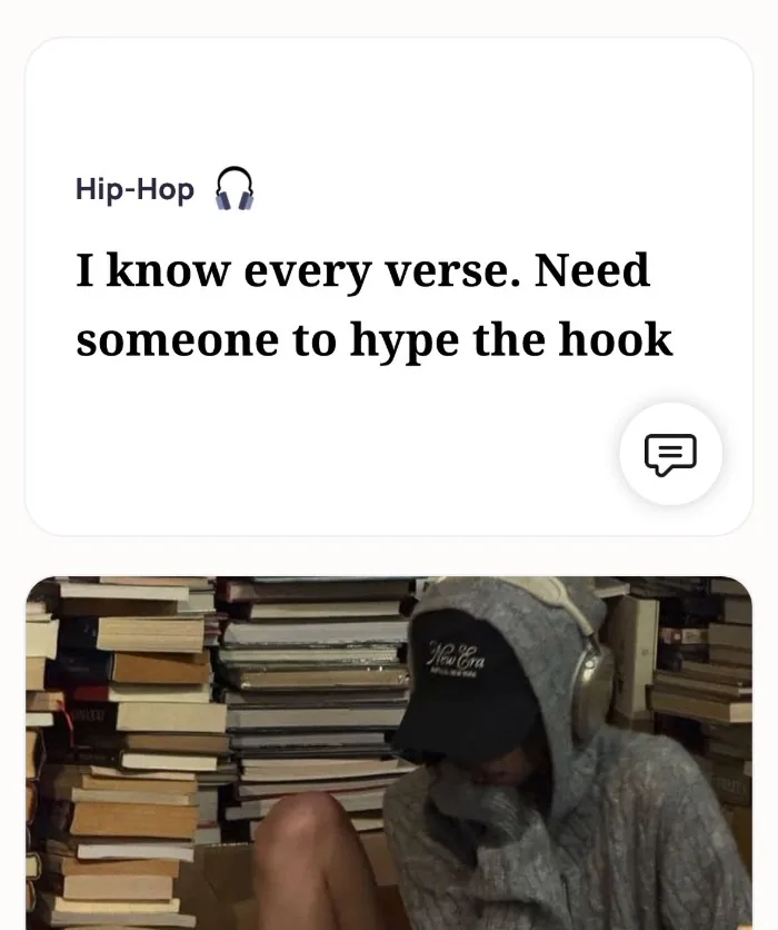 An Alyke profile card for Hip-Hop that reads: I know every verse. Need someone to hype the hook, above a photo of the member in a hoodie, cap and headphones sitting among stacks of books