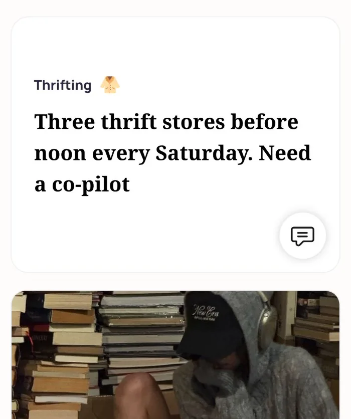 An Alyke profile card for Thrifting that reads: Three thrift stores before noon every Saturday. Need a co-pilot, above a photo of the member in a gray hoodie and cap reading at a small table among stacks of books