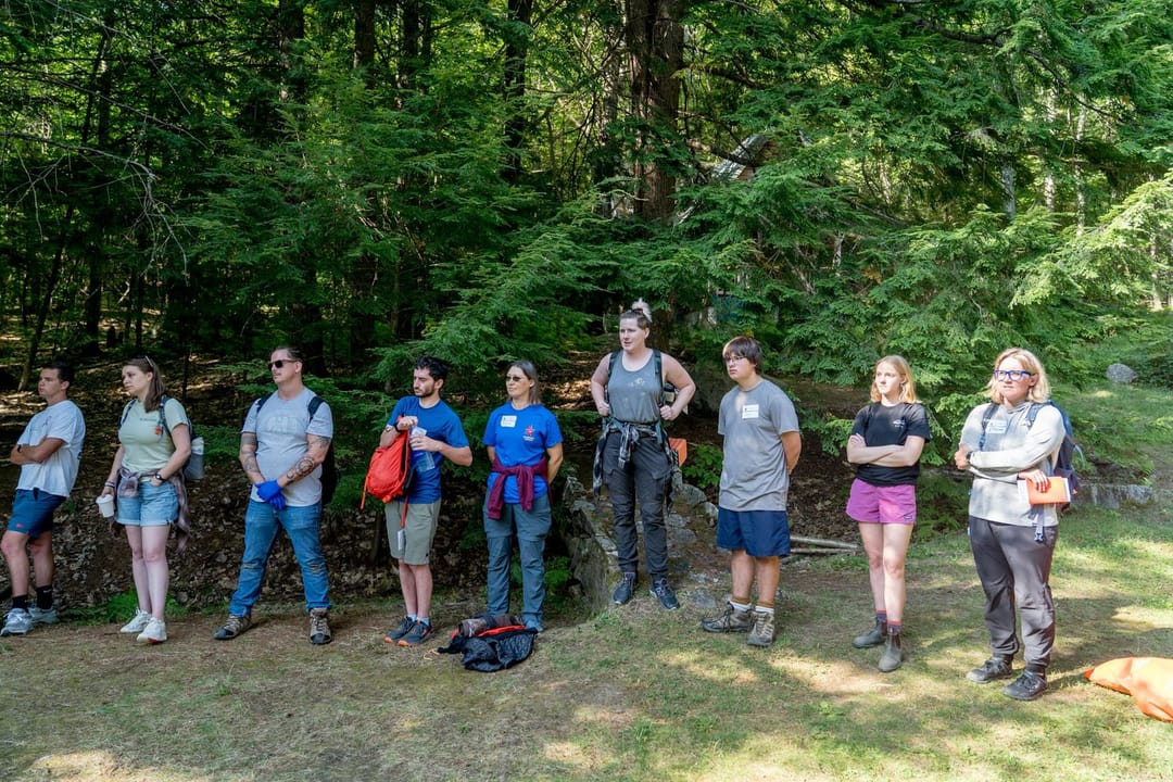 A hiking instructor helping beginners adjust their packs at a trailhead