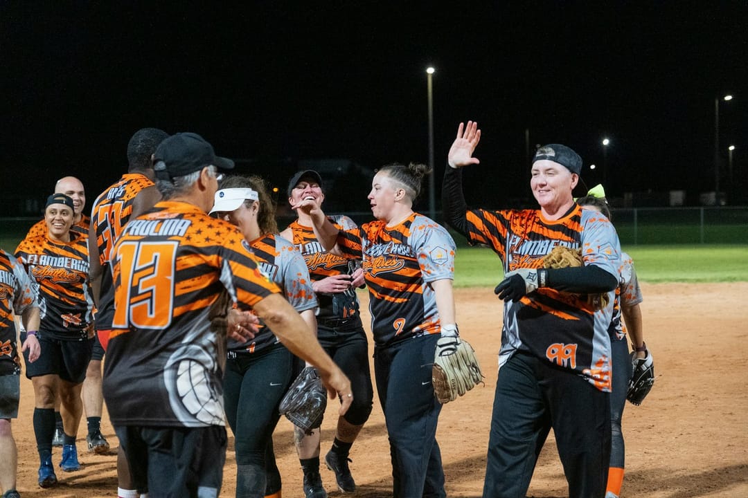 A kickball team high-fiving on a lit field