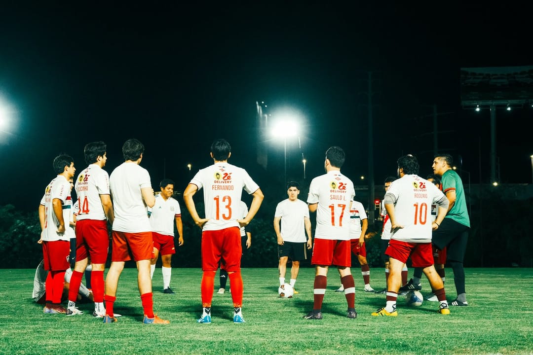 A kickball team laughing at home plate under lights