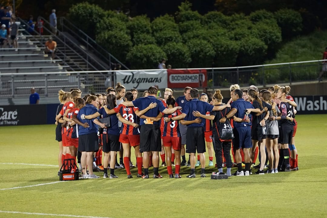 A kickball team laughing in a huddle on a floodlit field
