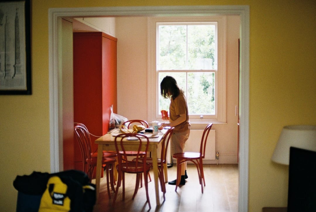 A remote worker eating lunch alone at a kitchen table, looking out the window