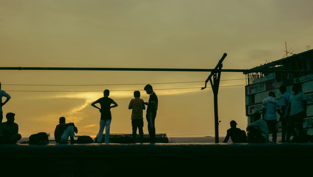 Runners talking while they stretch at a park corner at dusk