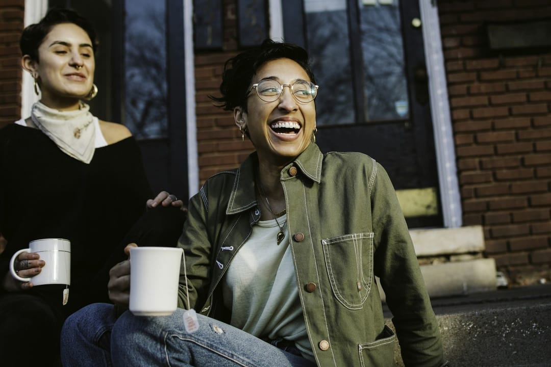 Two classmates laughing over a lopsided mug as they leave a pottery class