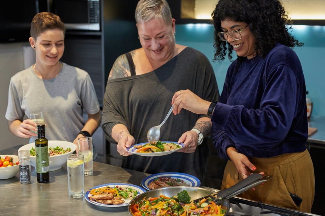 Two friends cooking together, one tasting from a spoon