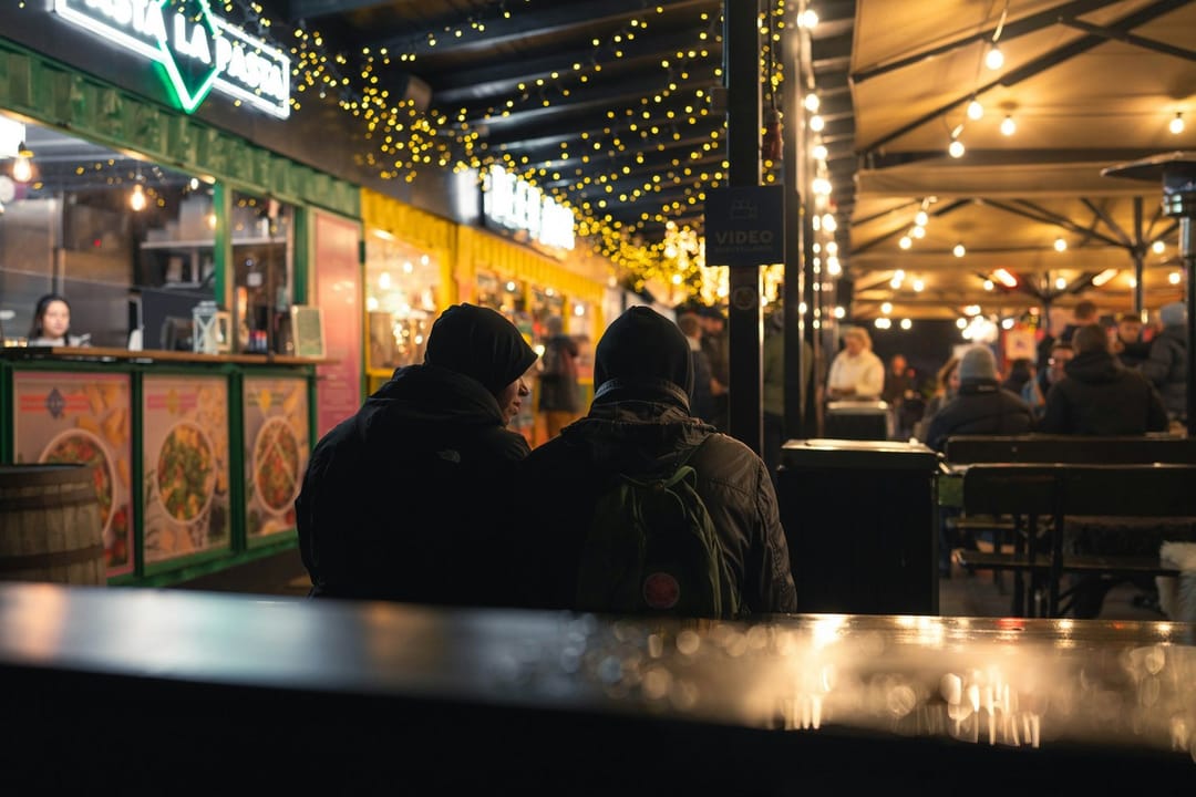 Two friends at an evening market under string lights