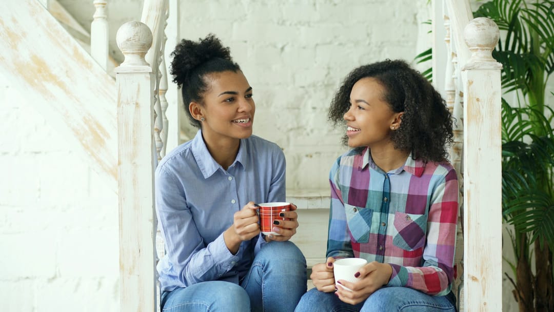 Two friends laughing with coffee on a brownstone stoop