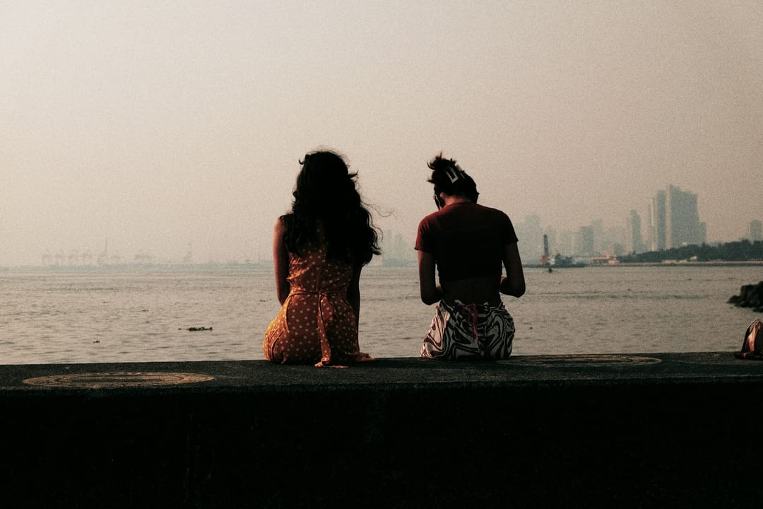 Two friends laughing over iced coffees on a lakeside path after work