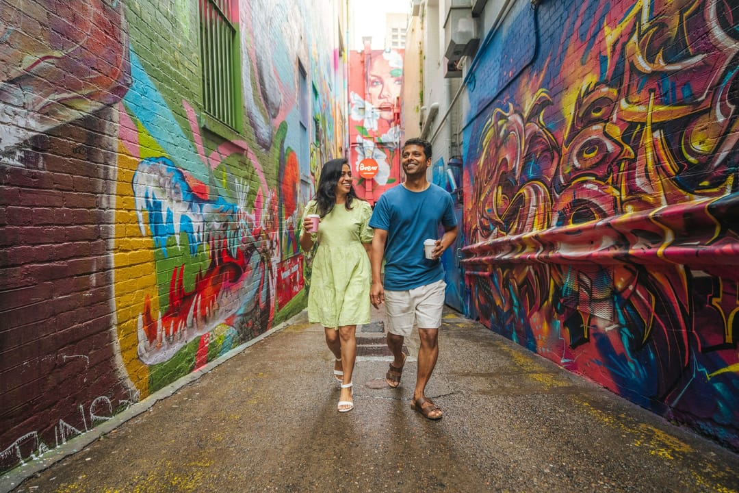 Two friends laughing on a mural-lined city trail at golden hour