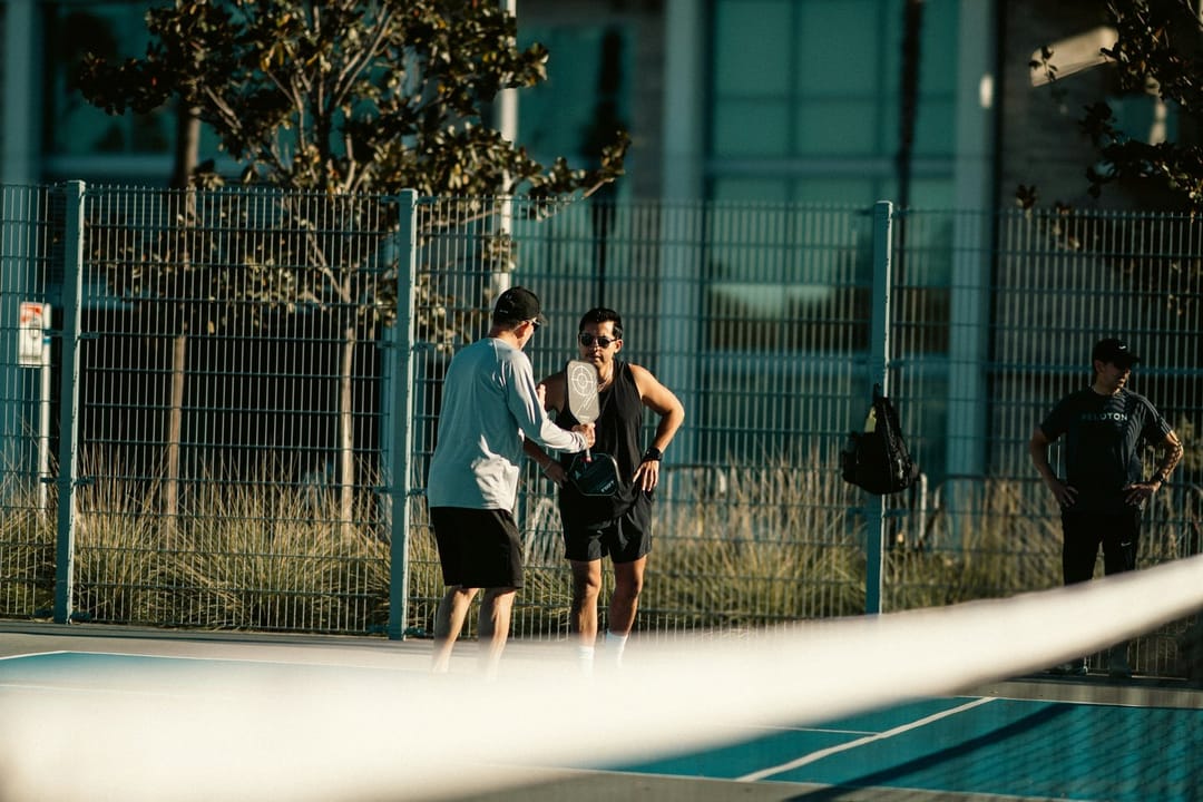 Two friends laughing on a pickleball court after a missed shot