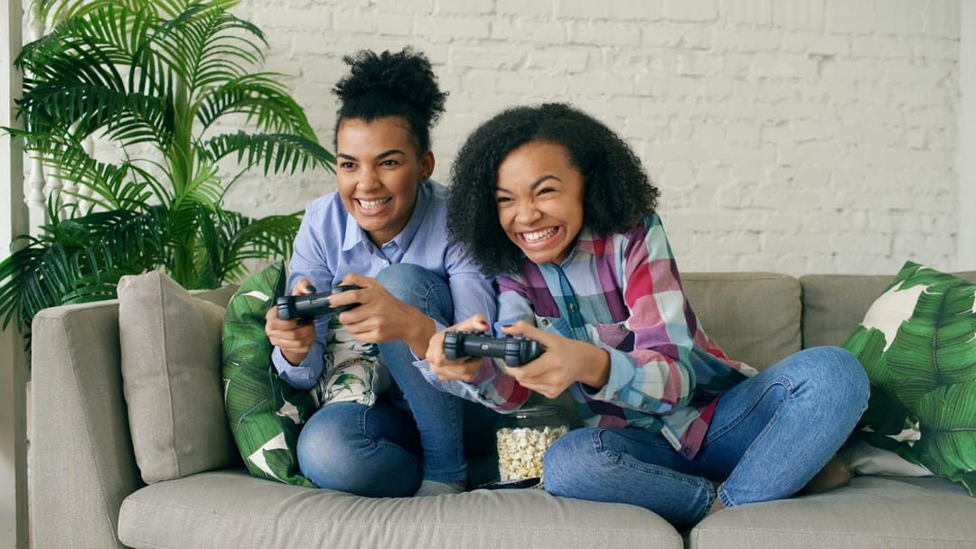Two friends laughing while playing a video game on a couch