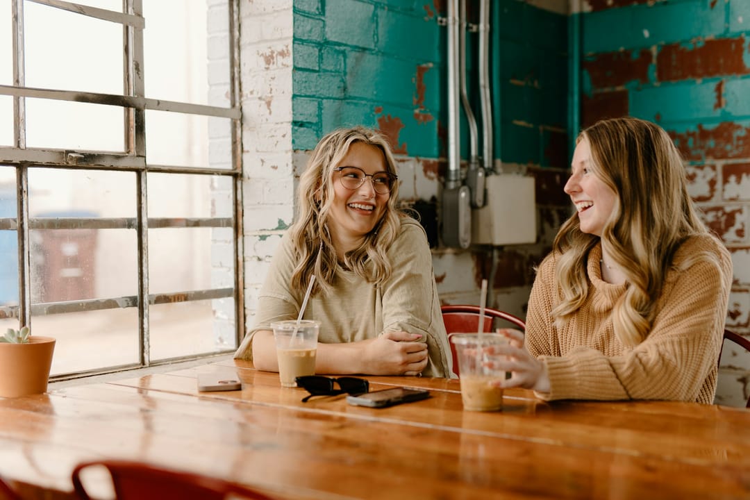 Two friends laughing under one umbrella outside a coffee shop