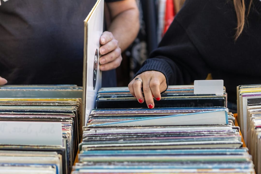 Two friends in a record store, one recognizing the album the other holds up