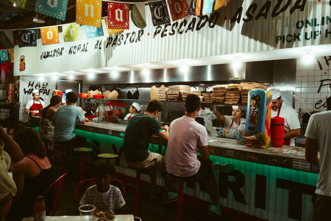 Two friends scoring tacos on a napkin at a taco truck at night
