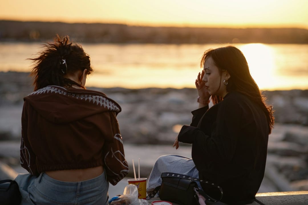 Two friends at a waterfront concert at dusk