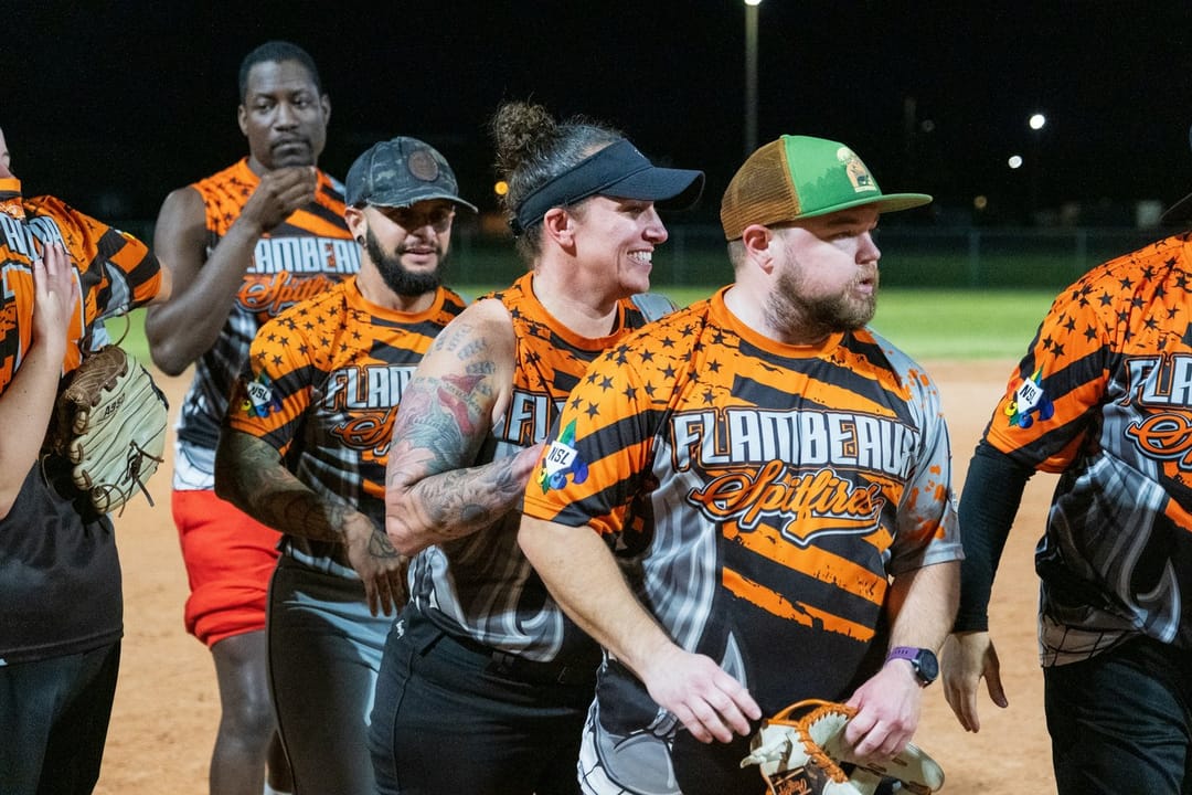Two kickball teammates laughing on the sideline under floodlights