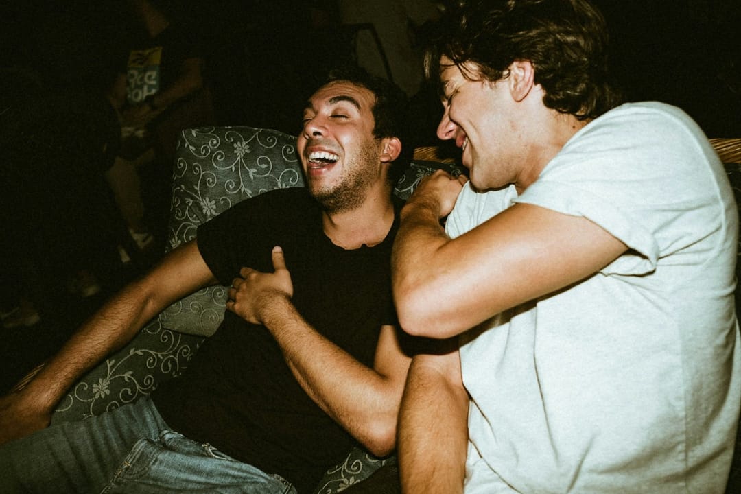 Two people laughing on the back steps of a house party