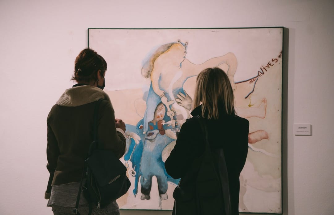 Two people talking in front of a painting at a gallery opening