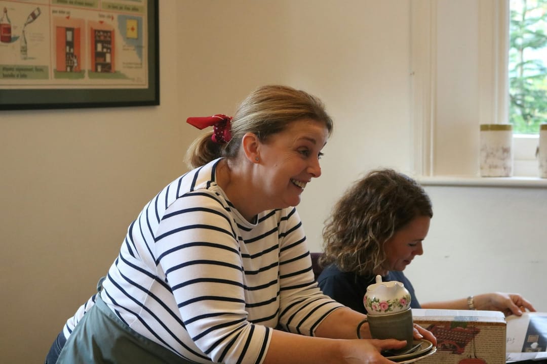 Two pottery class students laughing over a lopsided bowl
