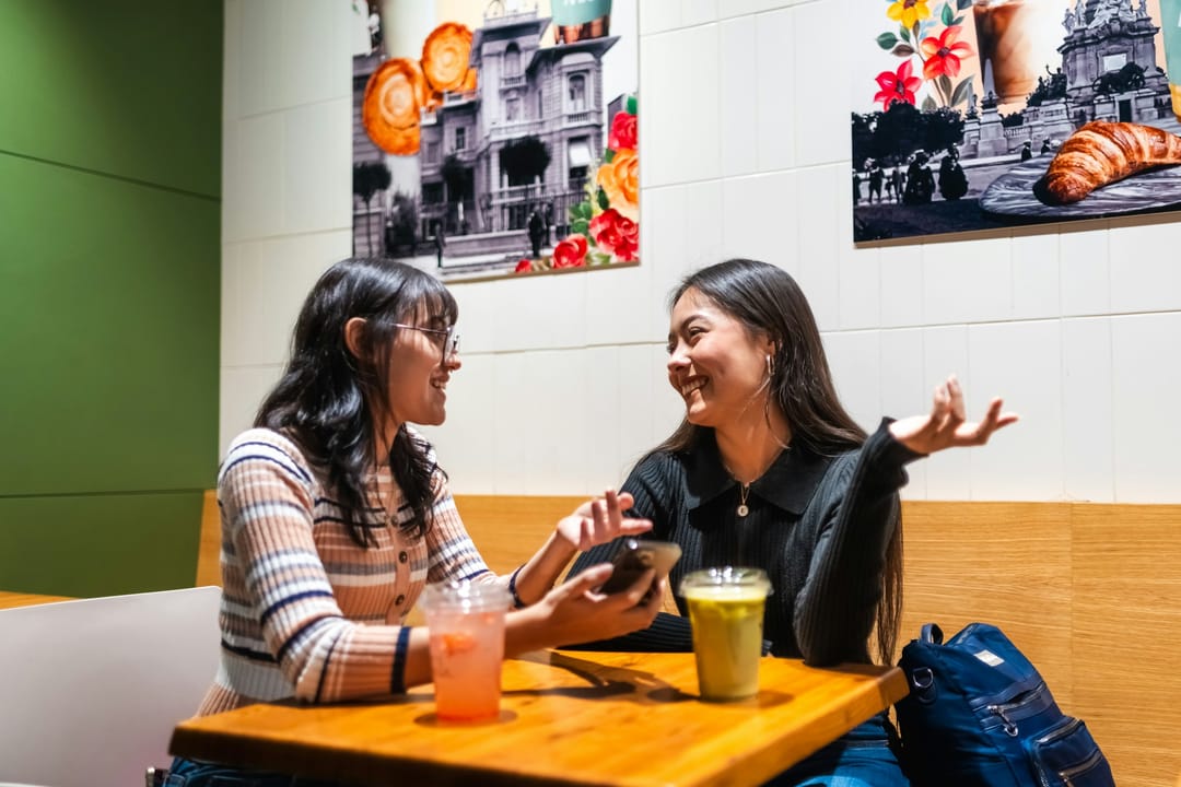 Two remote workers laughing at a shared cafe table on a weekday afternoon