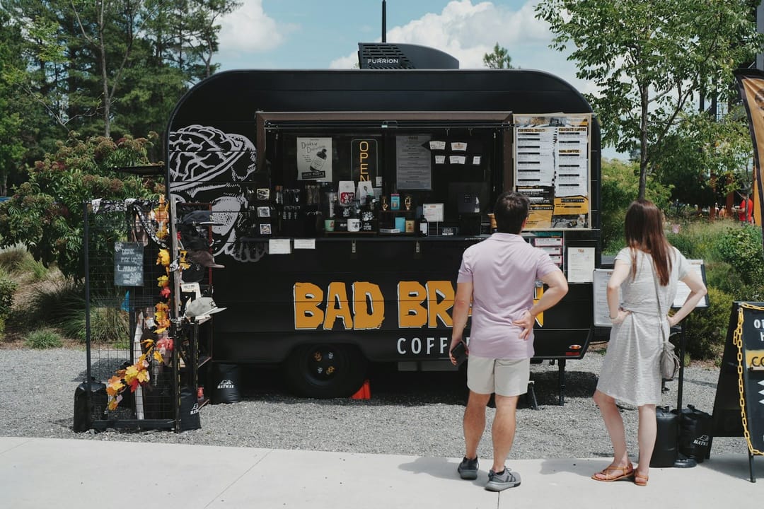 Two strangers talking in line at a food truck, one pointing at the menu