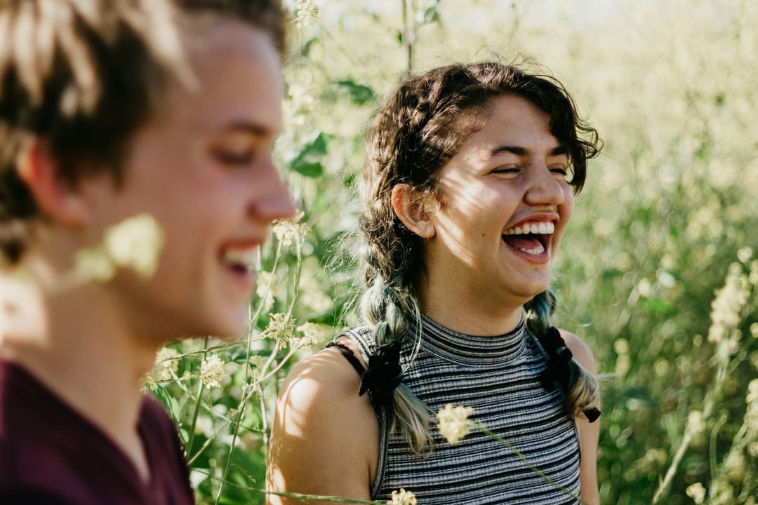 Two volunteers laughing as they pass a tray of seedlings in a community garden