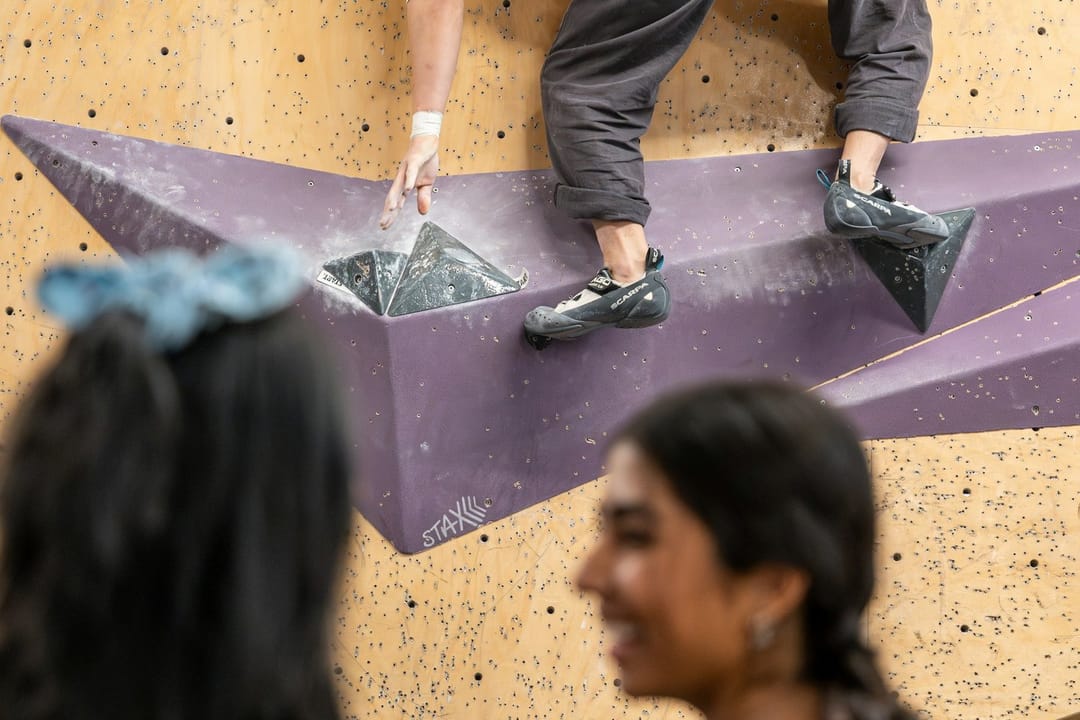 A woman laughing halfway up a climbing wall while a friend belays below