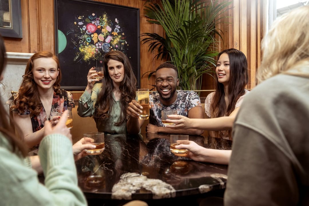 A young man at the edge of a laughing group of coworkers at a bar